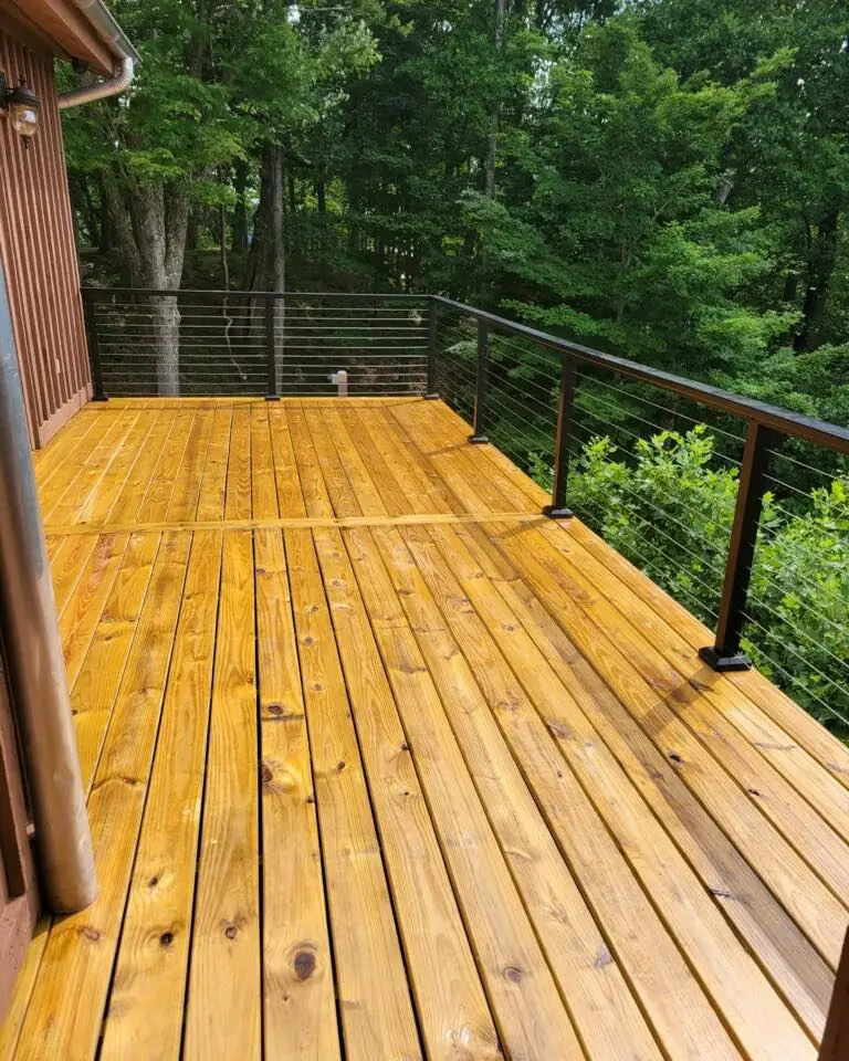 Golden stained wood deck with black cable railing above a lush forest